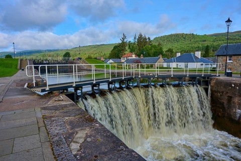 A waterfall in a lock surrounded by buildings and vegetation, Caledonian Canal, Fort Augustus, Loch