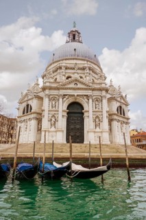 Majestic Venice church with intricate architecture reflects in calm waters. Gondolas line the canal