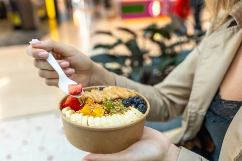 Woman holding and eating an acai bowl filled with fresh strawberries, bananas, blueberries, kiwi,