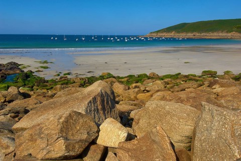 Quiet beach with many boats on the blue sea and rocks in the foreground, Brittany, France