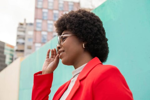 A woman in a vibrant red blazer confidently poses outdoors, set against an urban backdrop. Her