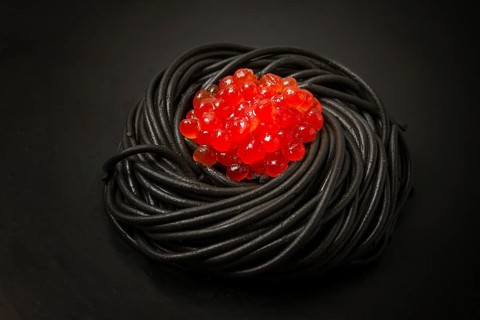 Black spaghetti with red caviar, pasta, on a black background, top view, no people
