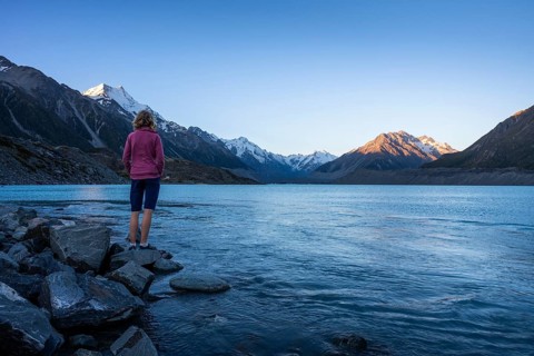 A woman is standing on the shores of Tasman Lake. On the left, Mount Cook. Golden hour. Aoraki