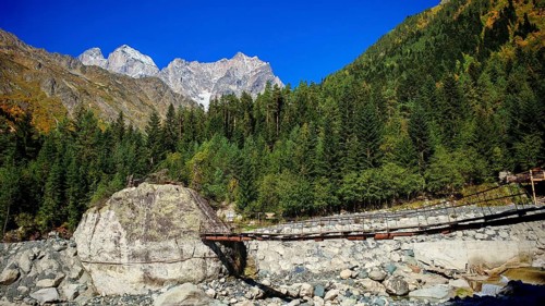 Suspension bridge over a rocky river surrounded by wooded mountain slopes and clear blue sky,