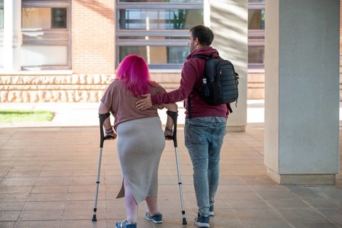 A supportive couple walks together in a college campus The woman, using crutches, has a disability