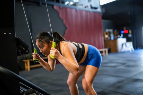 Side view of a Chinese woman exercising using lat machine pulling weights in a cross training gym