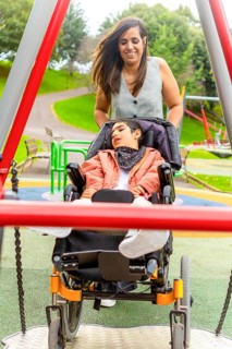 A mother joyfully pushes her child with cerebral palsy in a wheelchair on a swing at an accessible