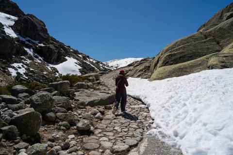 An Asian woman journeys on a snow-kissed path in Sierra de Gredos, Spain, surrounded by rugged