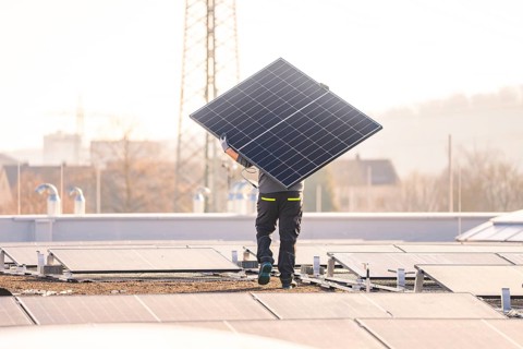 Technician carries a solar panel for installation on a roof in an urban environment, PV assembly at