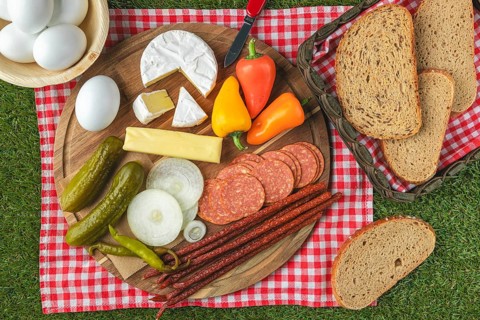 Board snack arranged on picnic blanket, vegan sausage, cheese, bread, eggs and peppers