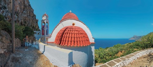 The red-domed church of Panagia Wrisiani is located on a rocky coast overlooking the blue sea under