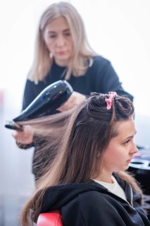 A hair stylist is drying a woman's hair with a blow dryer during a keratin hair treatment at a