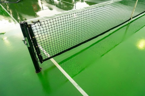 Pickleball court net standing on a vibrant green court surface wet from recent rain, reflecting
