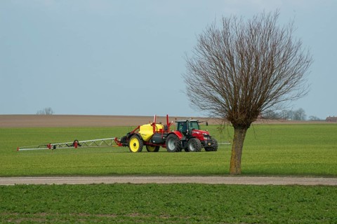 Spring farming, spreading fertilizer on a field with crops with a tractor at a willow tree in Ystad