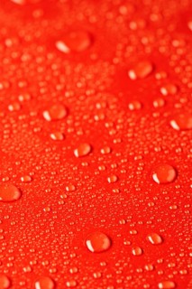 Close up of water droplets scattered on a vibrant red textured surface, creating a fresh and