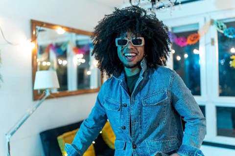 Portrait of a happy young latin man with curly hair and sunglasses smiling in a home night party