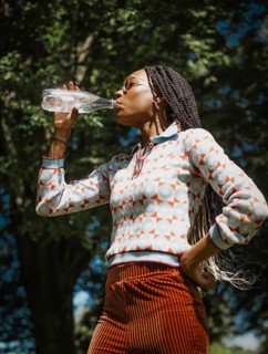A woman enjoys a summer day in nature, refreshing herself by drinking water. She is capturing