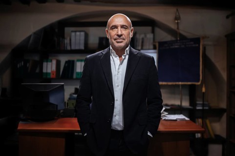 A confident businessman stands in a professional office setting. The background features shelves