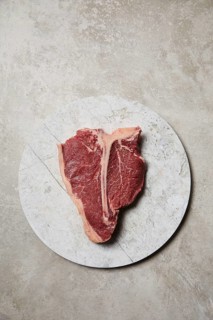 Freshly cut t-bone steak presented on a round marble plate, showcasing its juicy marbling and rich