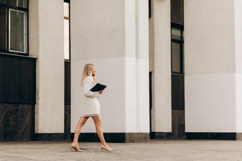 A business professional in formal attire confidently walks holding a folder, set against a modern