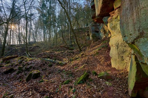 Rock formation in the forest with incoming sun rays and moss-covered soil, old quarry, Boxtal,