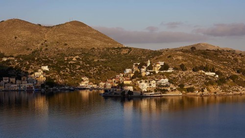 Coastal landscape with houses on the hill, illuminated by warm sunlight, calm water in the