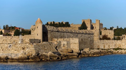 Massive fortress wall with battlements rises near the water, Rhodes Old Town, Rhodes, Dodecanese,