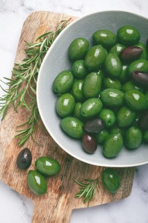 Chalkidiki olives, classic Greek green olives, in a bowl on a cutting board, top view, without