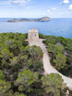 Historic defence defence tower Torre d'en Valls on a tree-covered hill overlooking the sea and the
