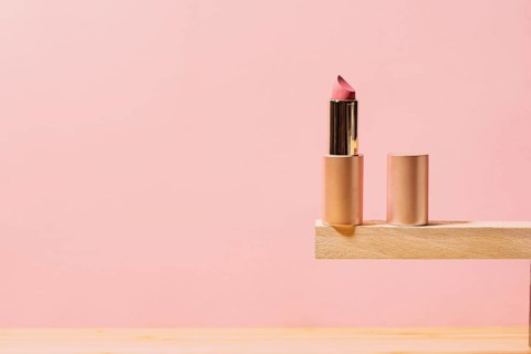 A stylish rose lipstick partially twisted up, placed on a wooden shelf with a pink background,