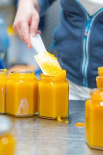 Person filling yellowish jam with a spatula into a hexagonal jar, jam production, Haselstaller Hof,