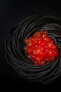 Black spaghetti with red caviar, pasta, on a black background, top view, no people