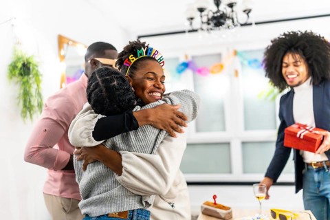 Latin young woman embracing multi-ethnic friends celebrating birthday party at home