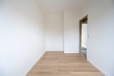Empty room is being renovated, walls are wallpapered, laminate on the floor, door opening without a