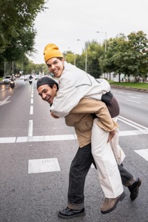 A cheerful Colombian gay couple shares a playful moment with a piggyback ride on a city street.
