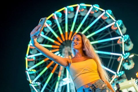 Woman taking a selfie next to ferris wheel at night enjoying in the amusement park
