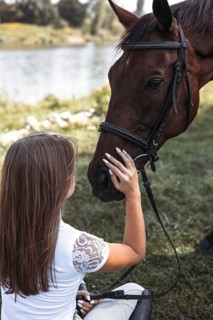 A young girl gently caresses a horse by a tranquil lakeside. The serene outdoor setting highlights