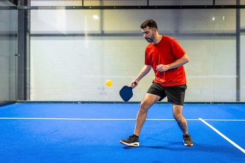 Active man playing pickleball on a vibrant blue indoor court, focused on striking a yellow ball