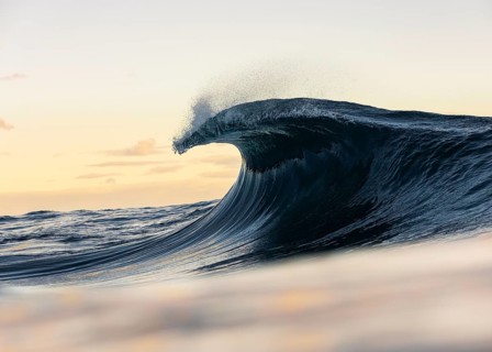 A mesmerizing ocean wave crests dramatically against the backdrop of a soft sunrise, capturing the