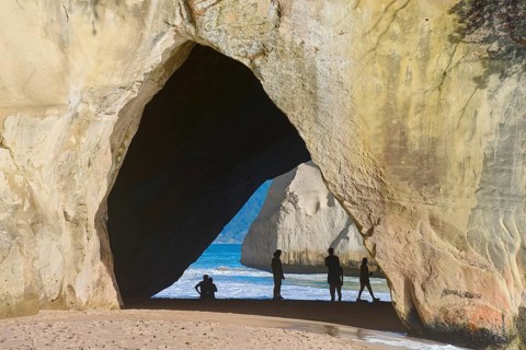 Natural rock formation with a view of the sea, people silhouetted in the cave on the sandy beach,