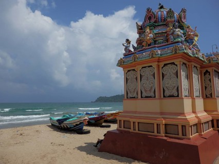 Several boats are moored on the beach next to an artfully designed Hindu temple, Thirukoneswaram