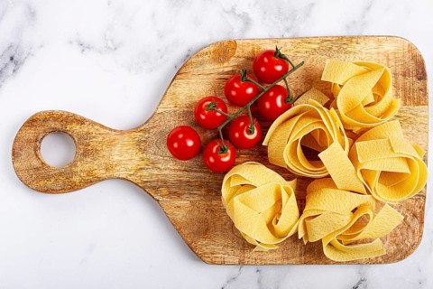 Raw pappardelle pasta, on a wooden chopping board, with cherry tomatoes, top view, no people