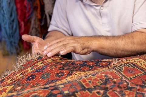 Cropped unrecognizable Iranian senior male artisan expertly restores a colorful, aged carpet in his