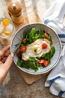Top view of a healthy lunch featuring fresh spinach leaves, cherry tomatoes, and a fried egg,