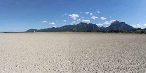 Cracked, dried out ground, waterless Forggensee in spring, behind it Tegelberg massif and Säuling,