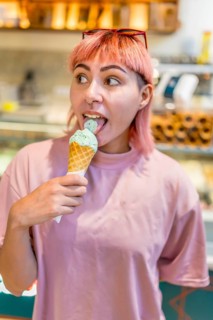 Vertical close-up portrait of a modern girl in pink hair eating ice cream in store