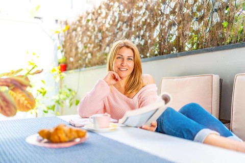 Adult caucasian blonde woman smiling at camera lying on a sofa in the outdoor yard enjoying
