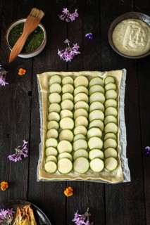 A beautifully arranged zucchini tart, complemented by vibrant edible flowers and bowls of green