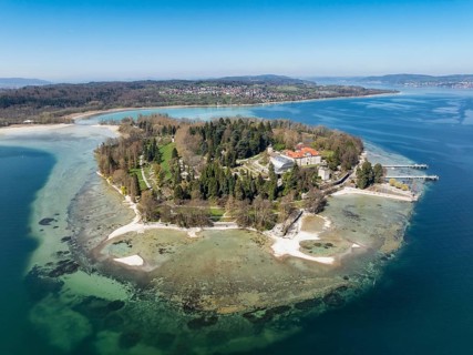 Aerial view of the island of Mainau at low tide with spring-like vegetation, on the horizon the