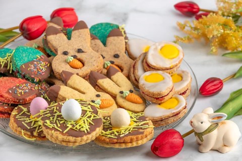 Plate of colourful Easter biscuits, decorated with carrots and eggs, next to red tulips